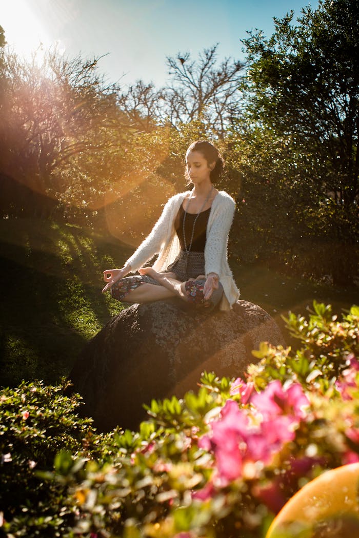 about-us Woman in tranquil meditation pose outdoors, bathed in sunlight, surrounded by lush greenery.