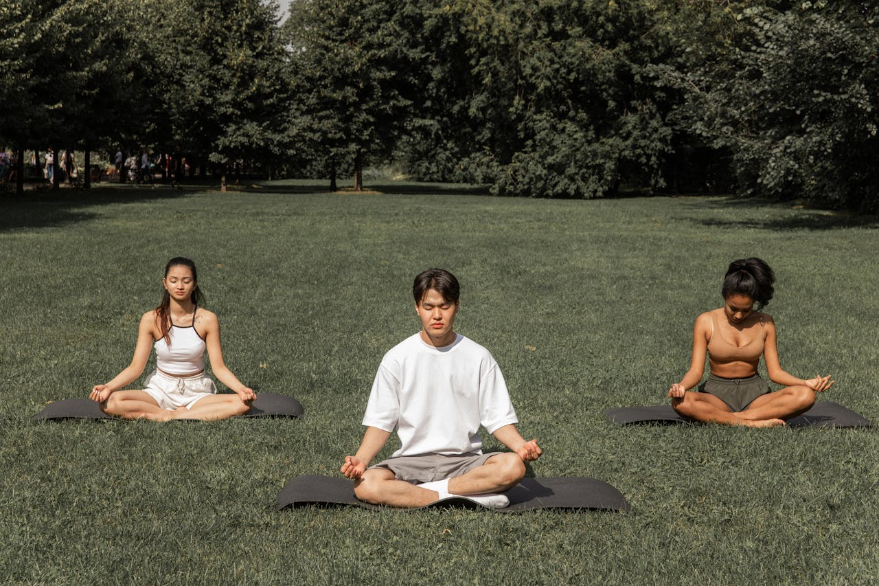 who-we-are Full length of peaceful people in sportswear sitting in Padmasana with closed eyes and meditating in summer garden