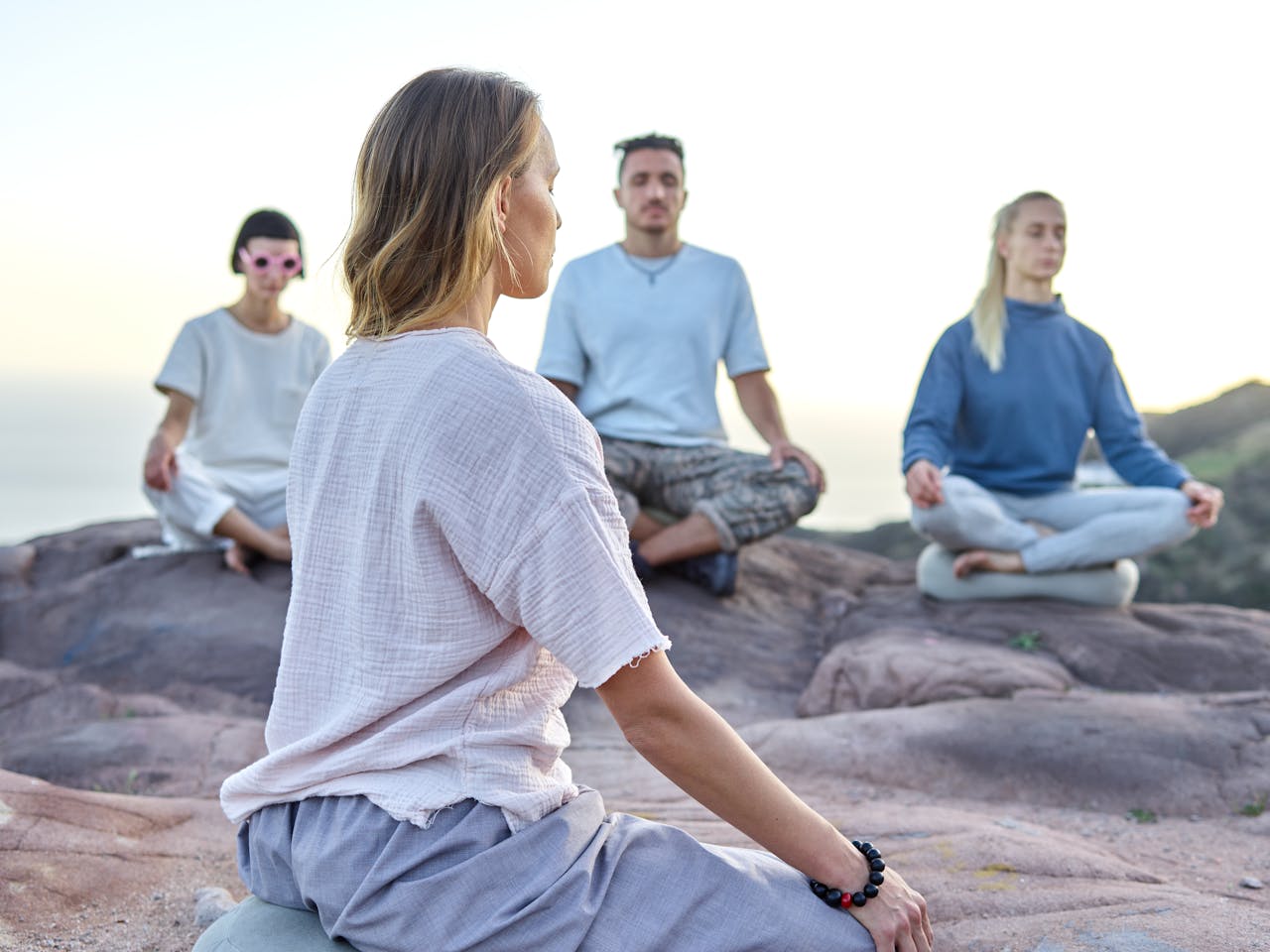Group of adults meditating on a rocky cliff at sunset, embracing relaxation and spirituality.